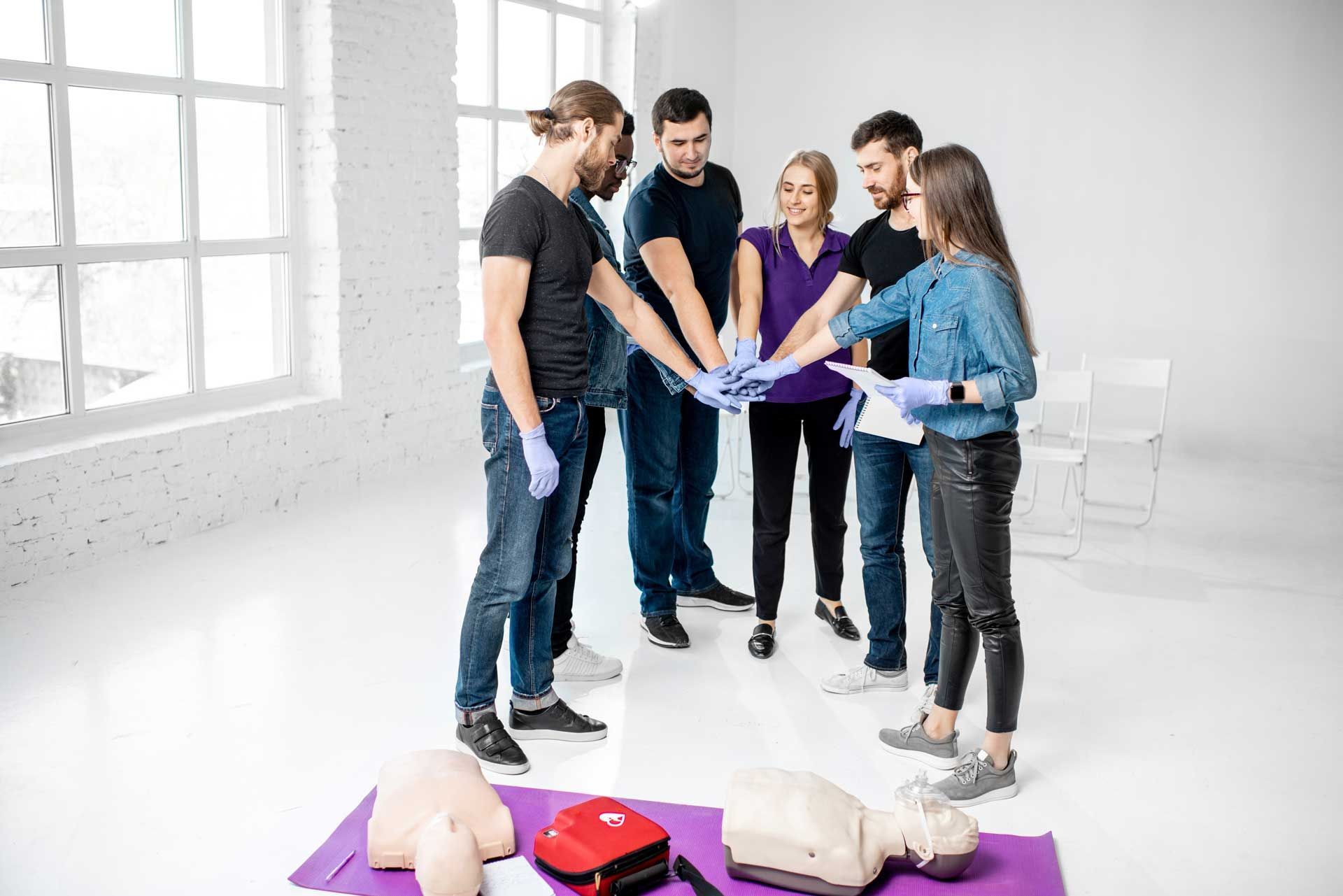 Group of people in training put hands together, CPR dummies and medical kit on mat.
