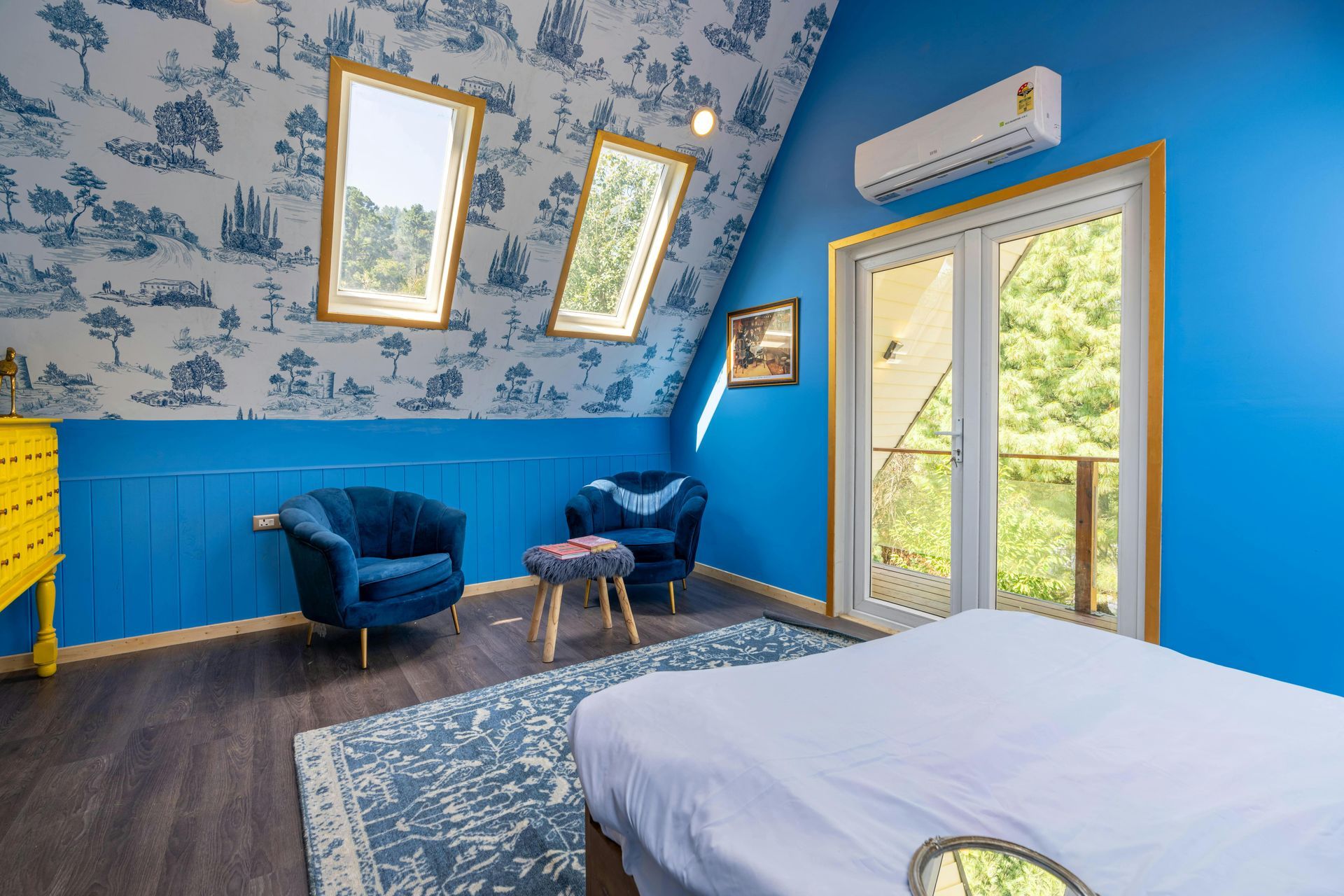 Bedroom with blue walls, patterned wallpaper, two armchairs, a bed, and a balcony.