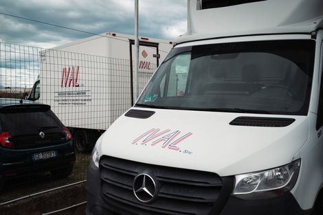 Un carrello elevatore Toyota arancione e un transpallet elettrico arancione più piccolo, entrambi parcheggiati in un corridoio di stoccaggio di un magazzino industriale.