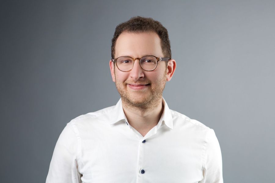 A man wearing glasses and a white shirt is smiling for the camera.