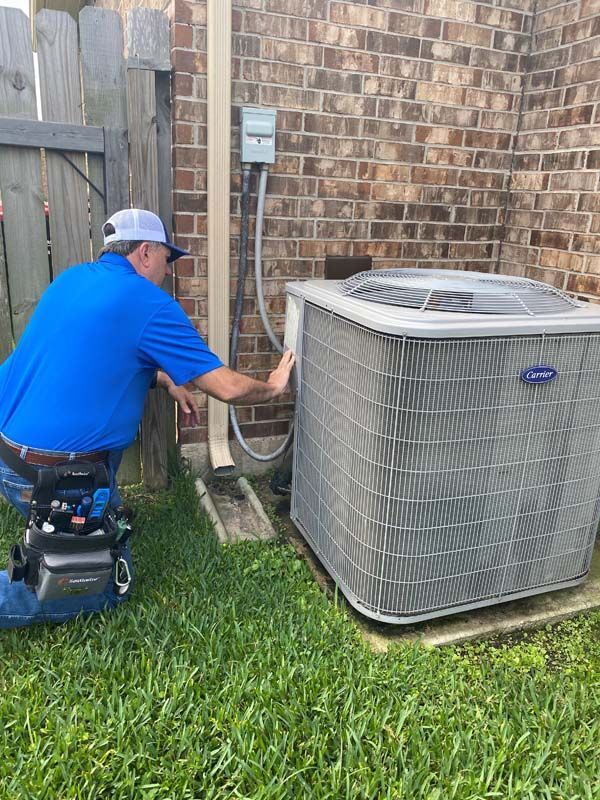 A man is kneeling down in front of an air conditioner.