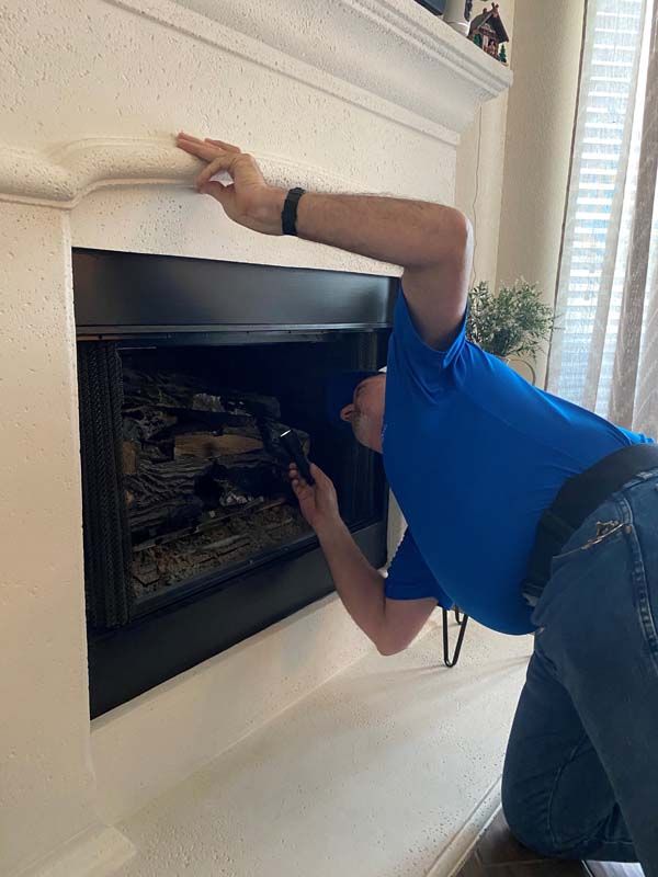 A man in a blue shirt is kneeling down in front of a fireplace.