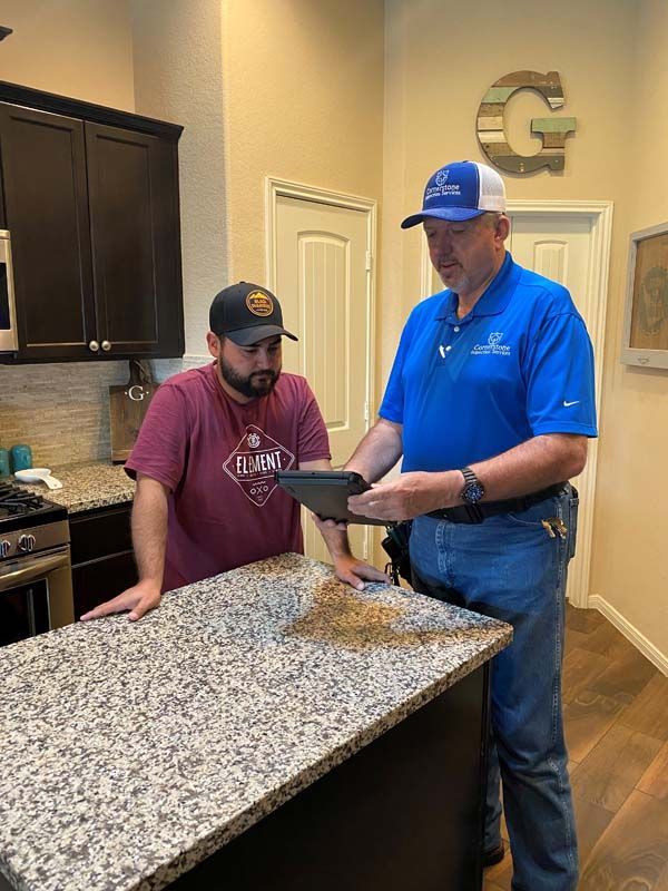 Two men are standing in a kitchen looking at a tablet.