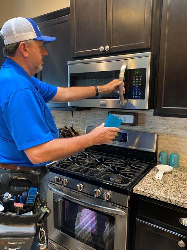 A man in a blue shirt is cleaning a microwave in a kitchen.