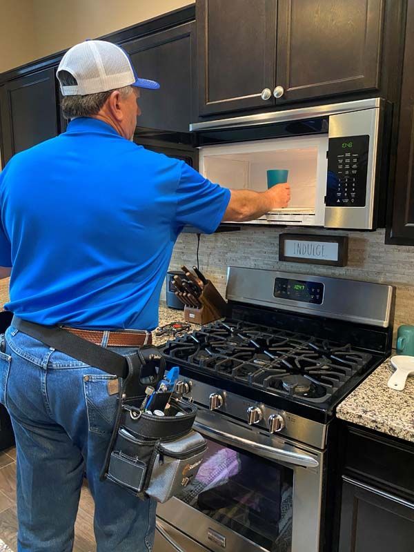 A man in a blue shirt is cleaning a microwave in a kitchen.