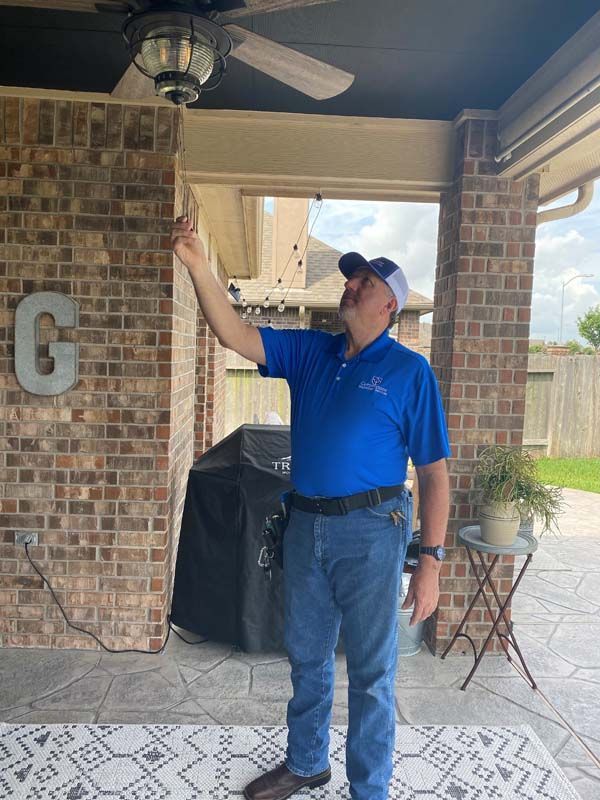 A man in a blue shirt is standing on a porch looking at a ceiling fan.