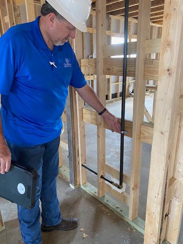 A man wearing a hard hat and a blue shirt is looking at a pipe