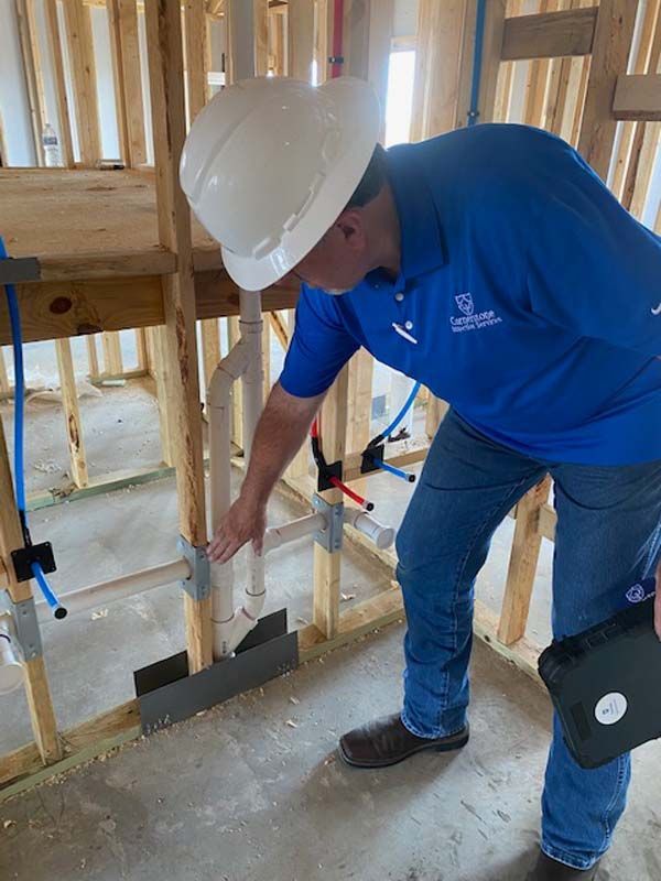 A man wearing a hard hat and a blue shirt is looking at a pipe.