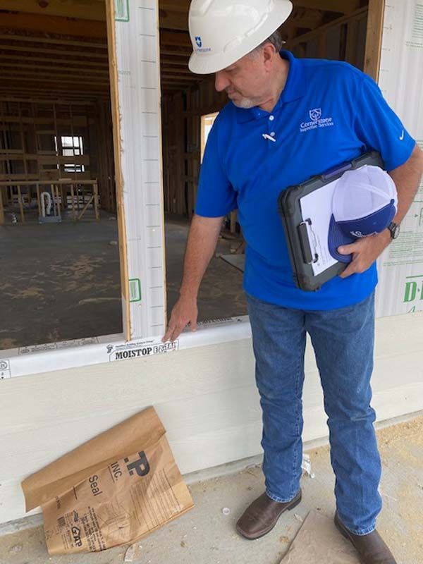 A man wearing a hard hat and a blue shirt is standing in front of a window.