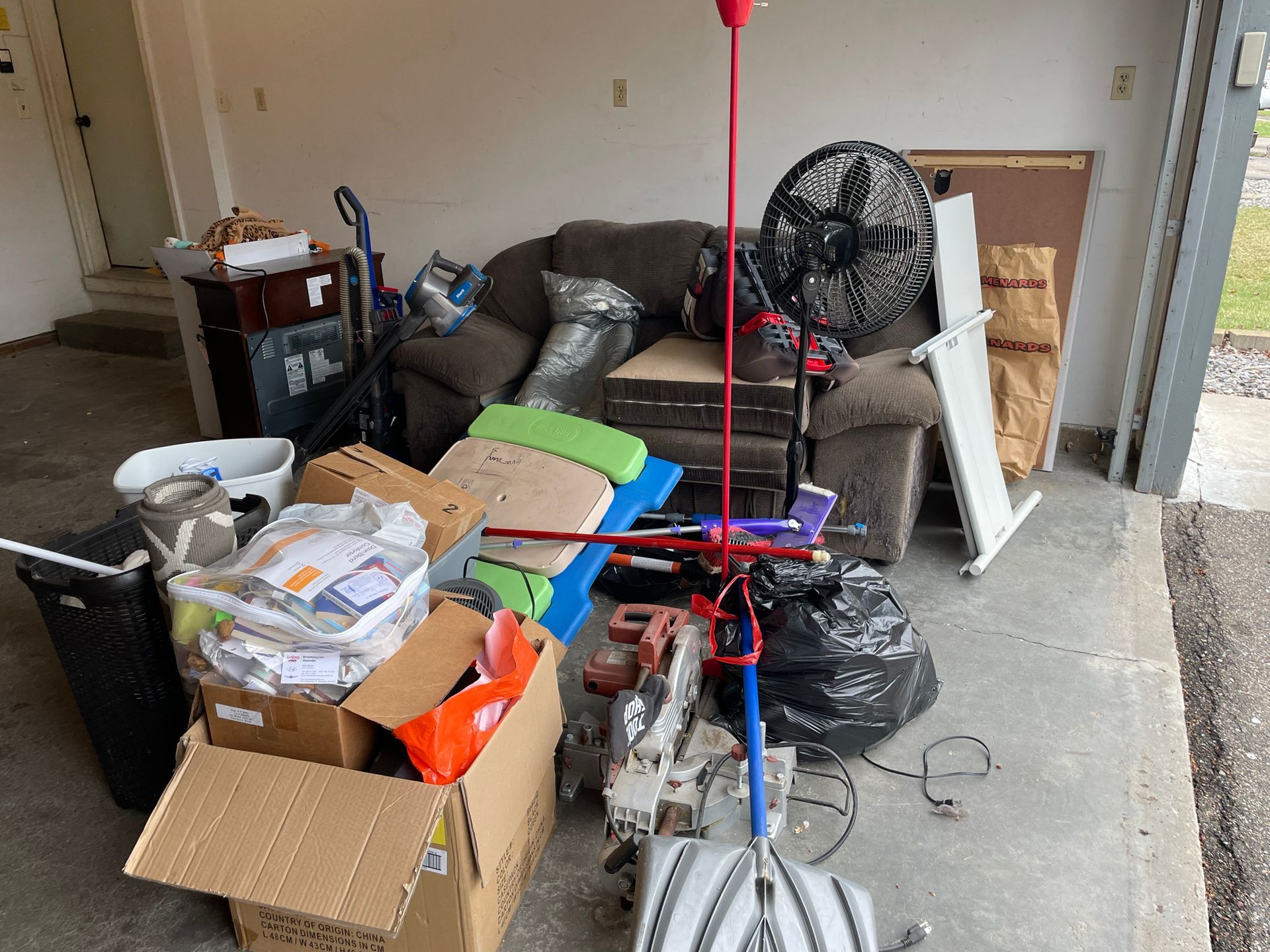 A garage filled with boxes , a couch , a fan , and other items.
