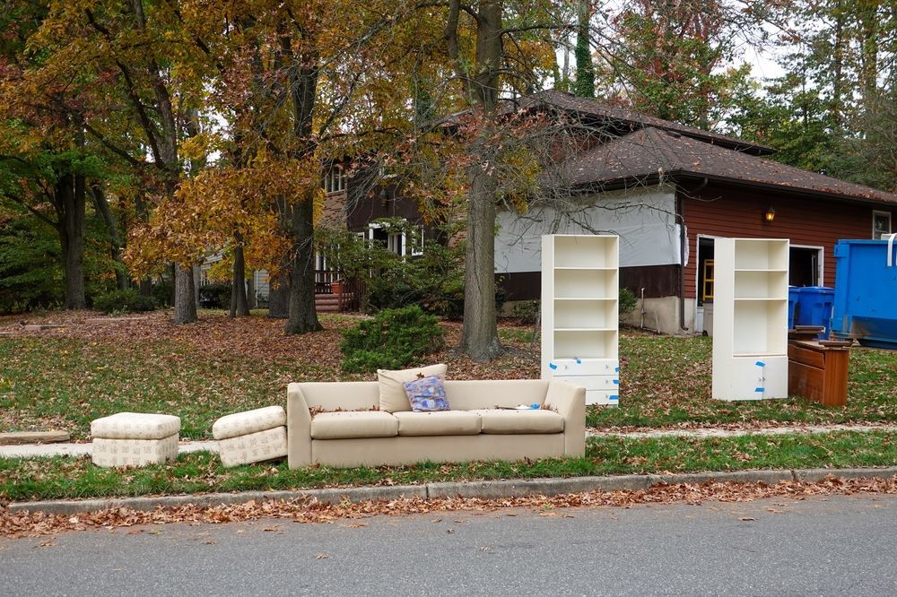 A couch and shelves are sitting on the side of the road in front of a house.