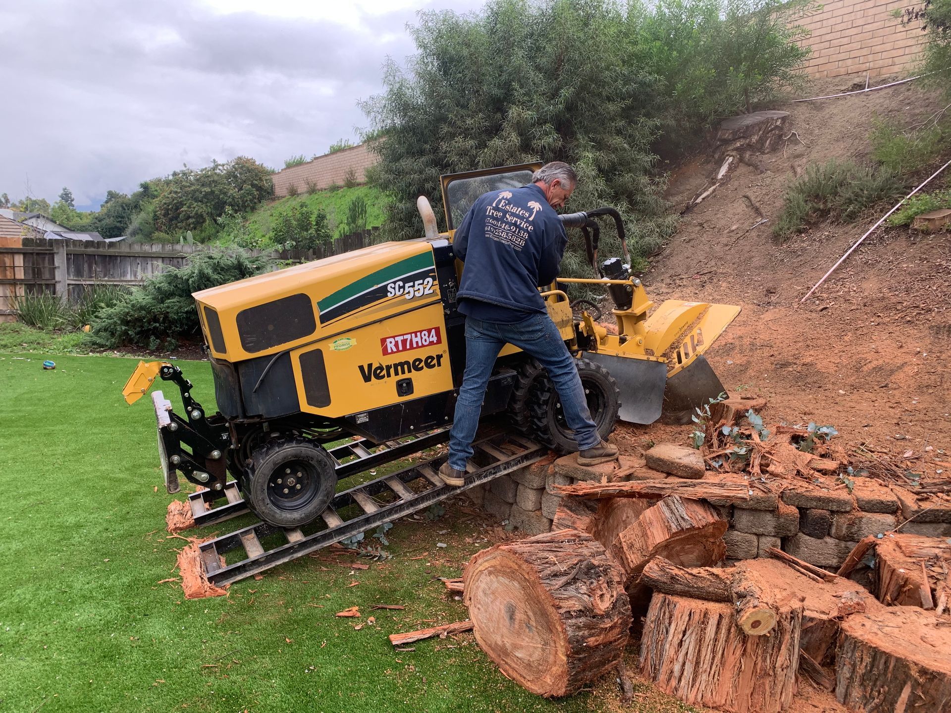 Man operating a Vermeer stump grinder on a sloped yard, grinding wood.