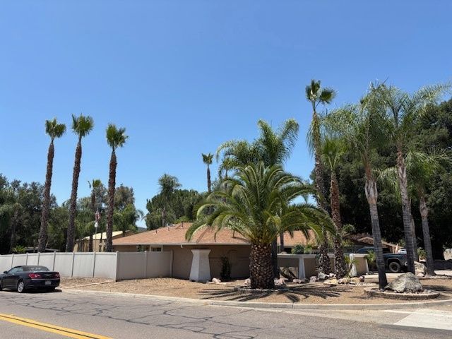 A car is parked in front of a house surrounded by palm trees