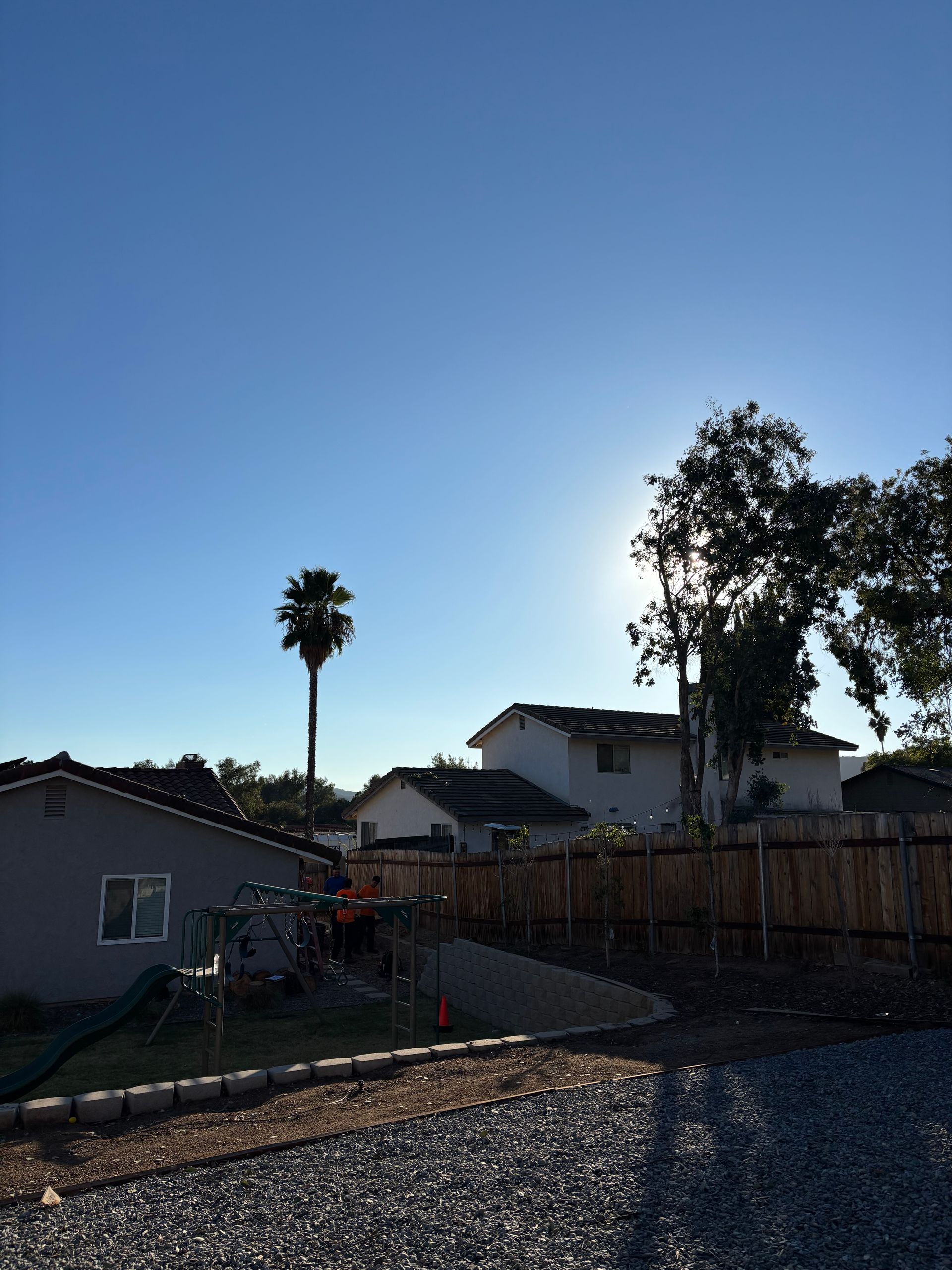 Palm trees frame a white coastal house on a hillside under a cloudy sky.