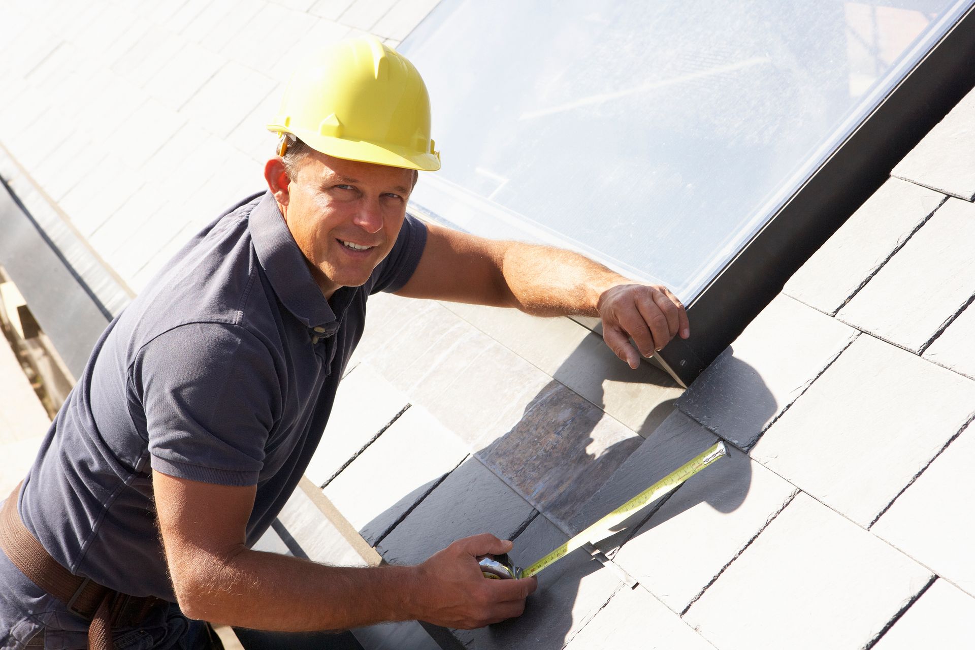 A man wearing a yellow hat is measuring a roof.