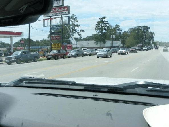 View from inside a car on a busy road with multiple vehicles and storefront signs ahead