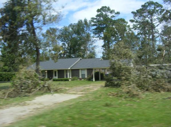 Single-story house with a front porch, surrounded by trees and a grassy yard.