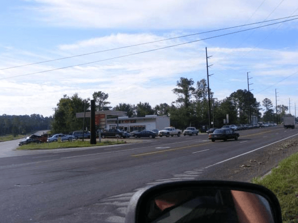 Roadside gas station and parking lot beside a busy multi-lane street under a clear sky