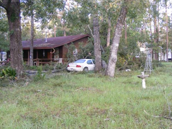 White car parked by a small house in a grassy wooded yard