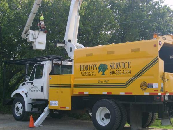 Yellow utility truck with raised bucket lift beside trees in a residential area