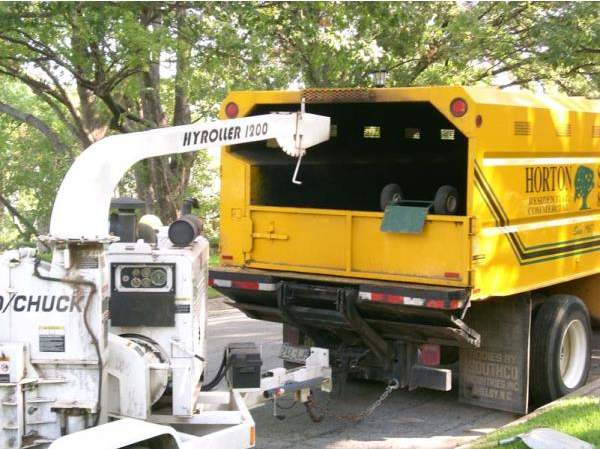 Tree trimmer loading branches into a yellow truck with a white hydraulic boom and chipper attachment