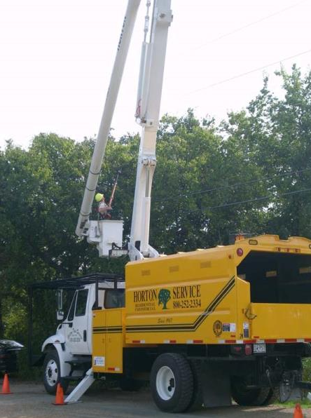 Yellow utility truck with extended boom lift raised beside trees on a street