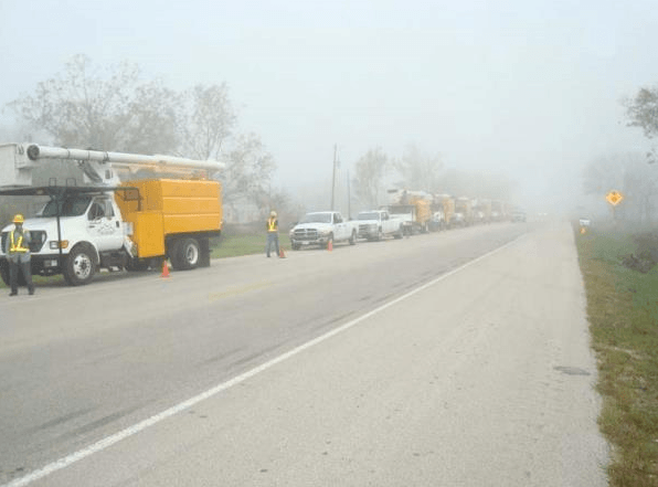 Foggy roadside scene with utility trucks and workers lining a rural road