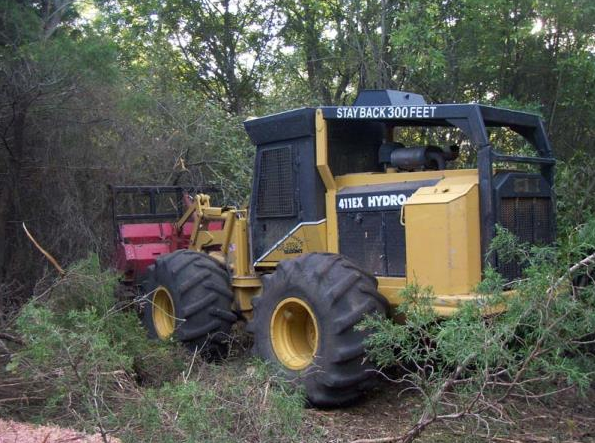 Yellow forestry machine clearing brush in a dense wooded area