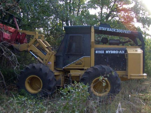 Yellow and black logging machine in a wooded area with a red attachment