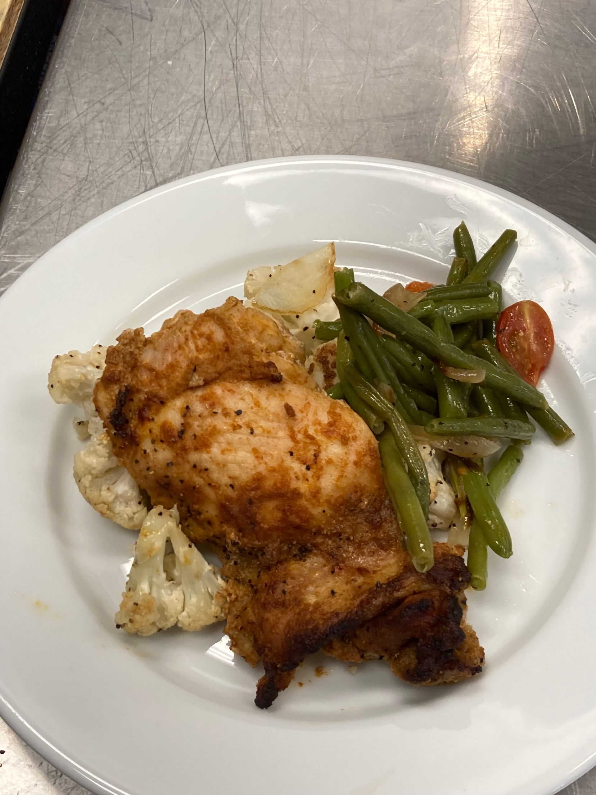Chicken breast with roasted cauliflower and green beans on a white plate.