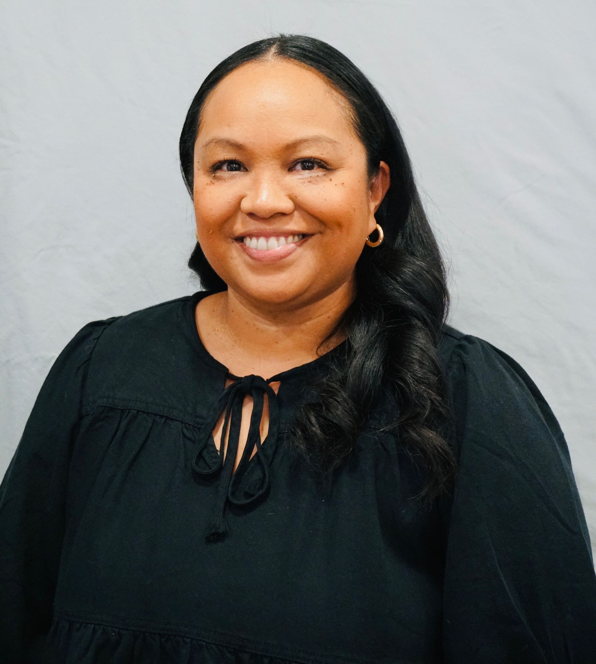 A woman wearing a black shirt and earrings is smiling for the camera.