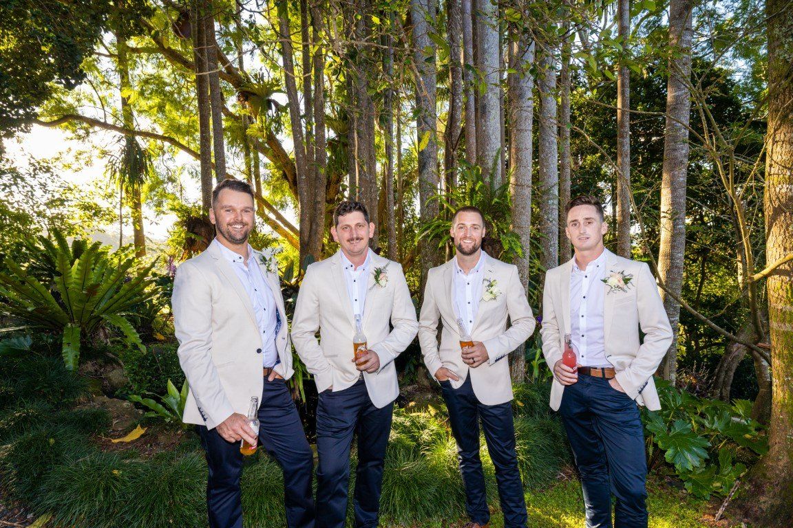the groom and his groomsmen are posing for a picture in the woods .