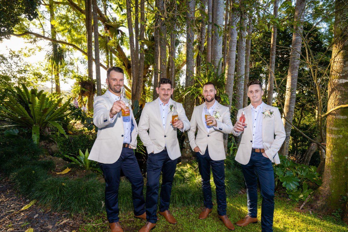 a group of men standing next to each other in a forest holding drinks .