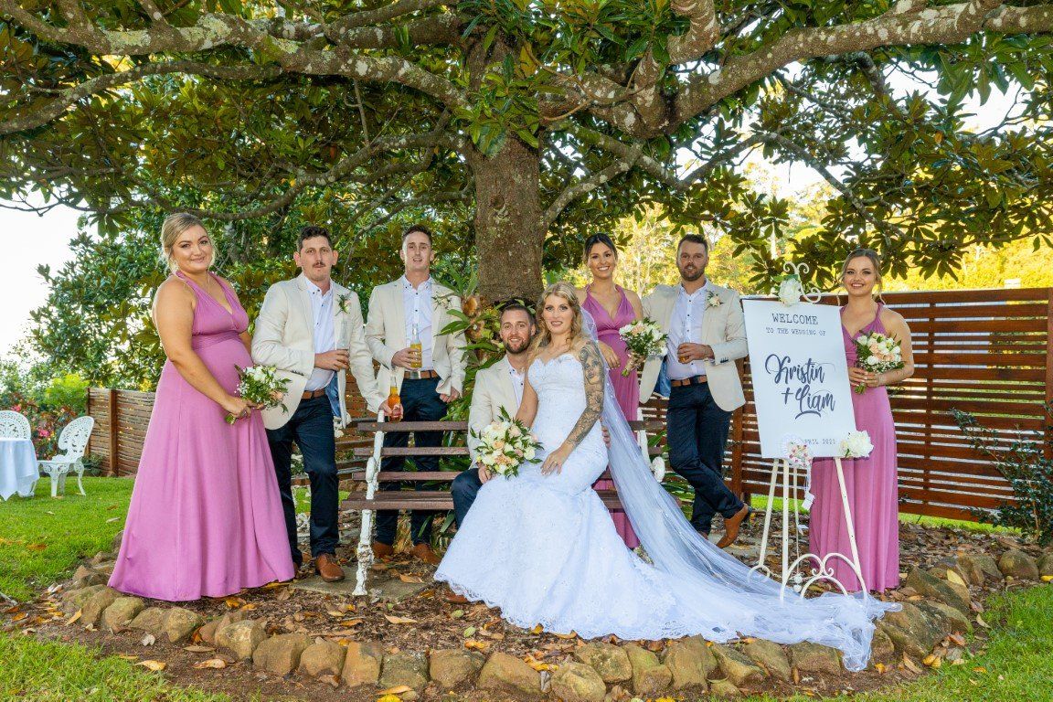 a bride and groom are posing for a picture with their wedding party under a tree .