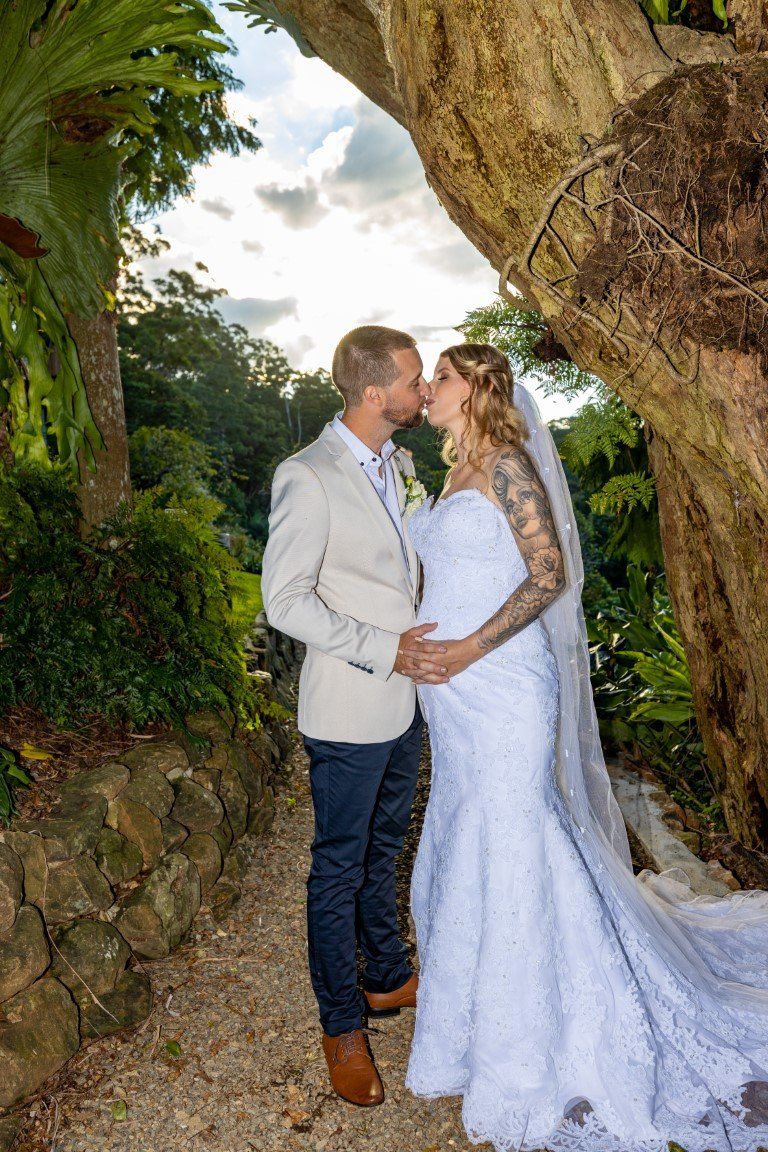 a bride and groom are kissing under a tree .