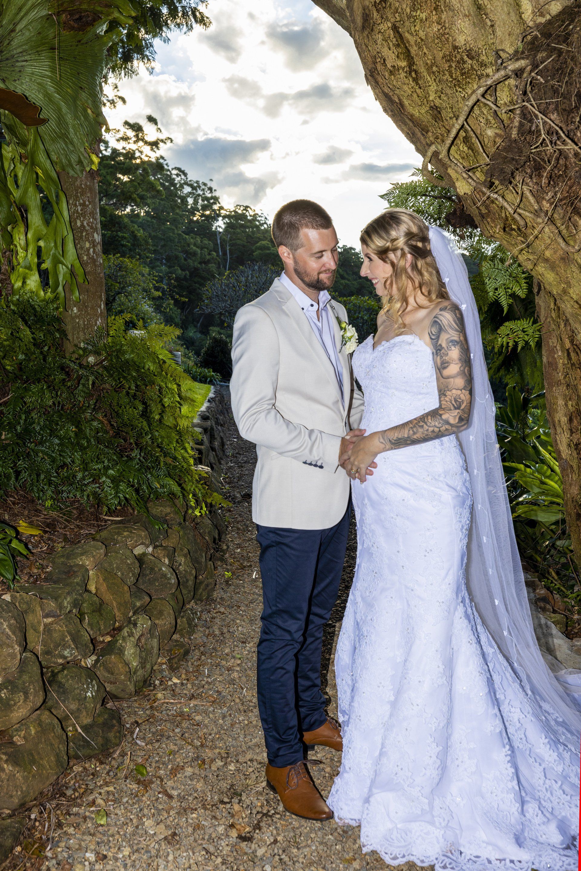 a bride and groom are standing next to each other under a tree .
