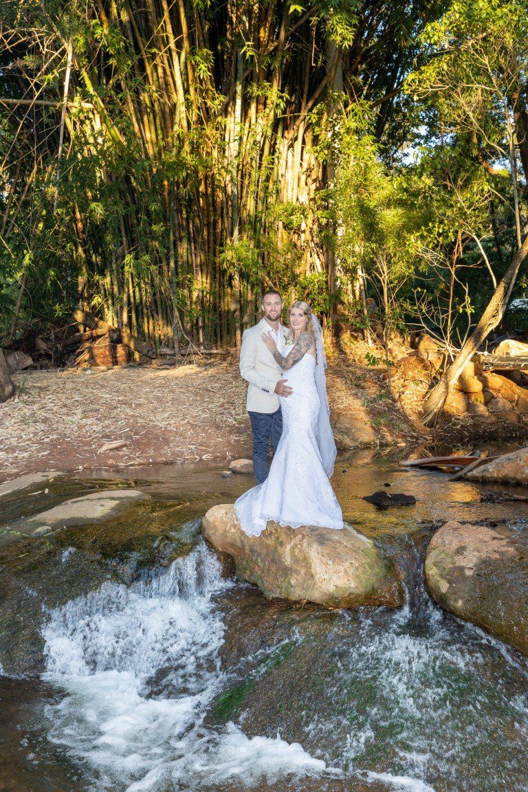 a bride and groom are standing on a rock in a river .