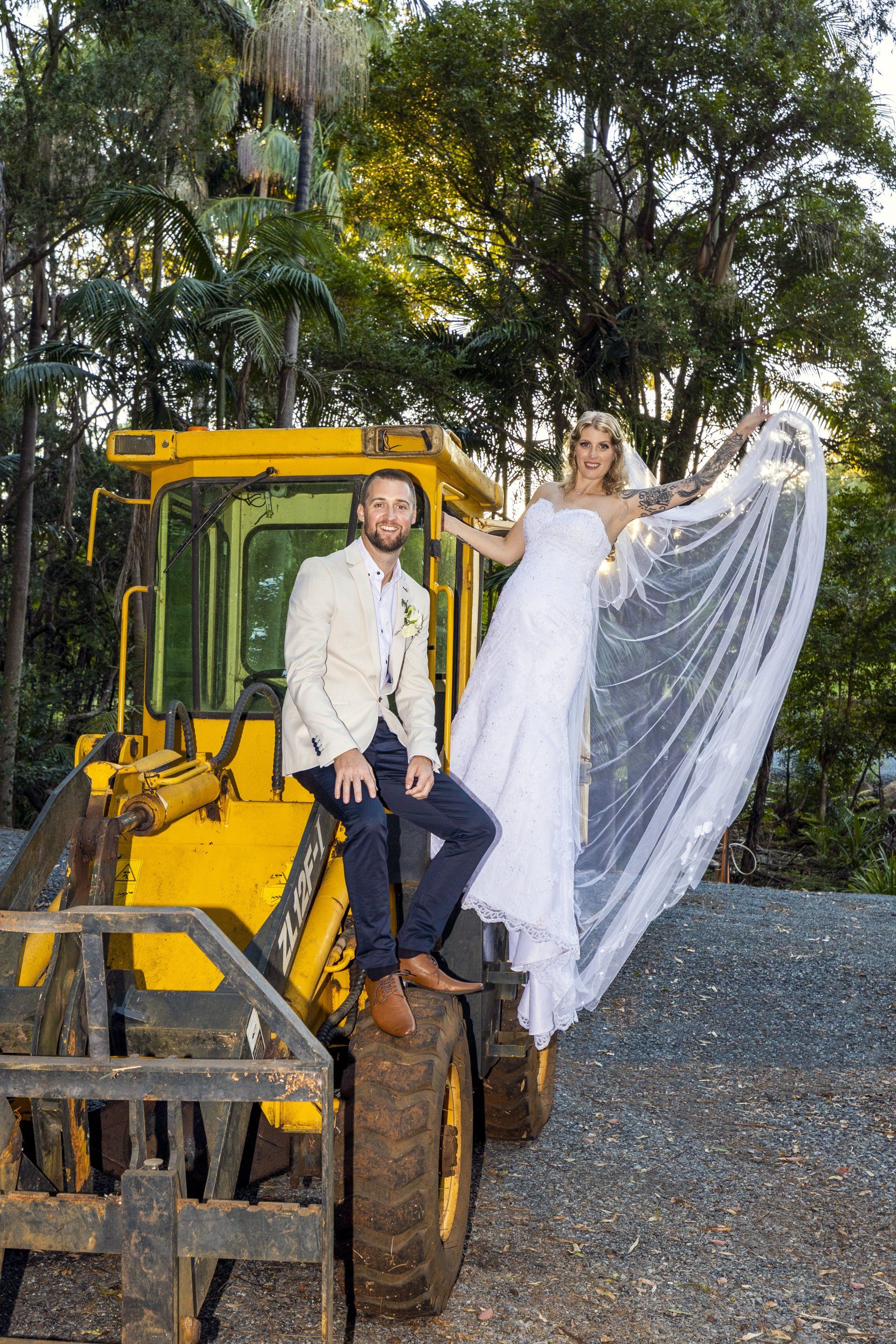 a bride and groom are sitting on top of a yellow tractor .
