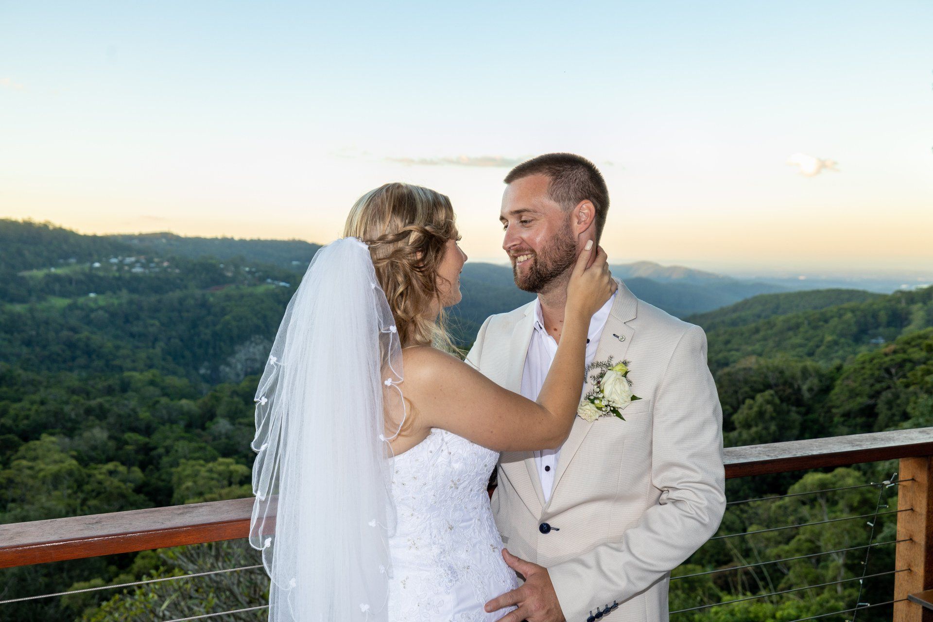 a bride and groom are standing next to each other on a balcony overlooking a forest .
