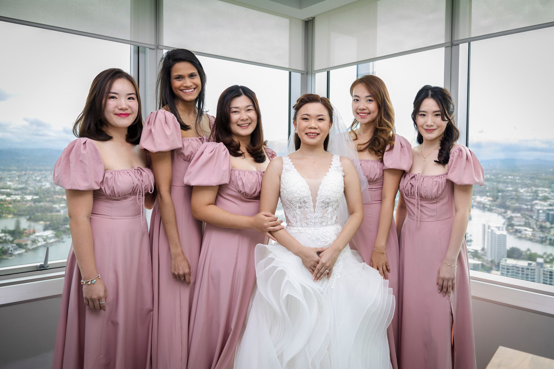 a bride and her bridesmaids are posing for a picture in front of a window .