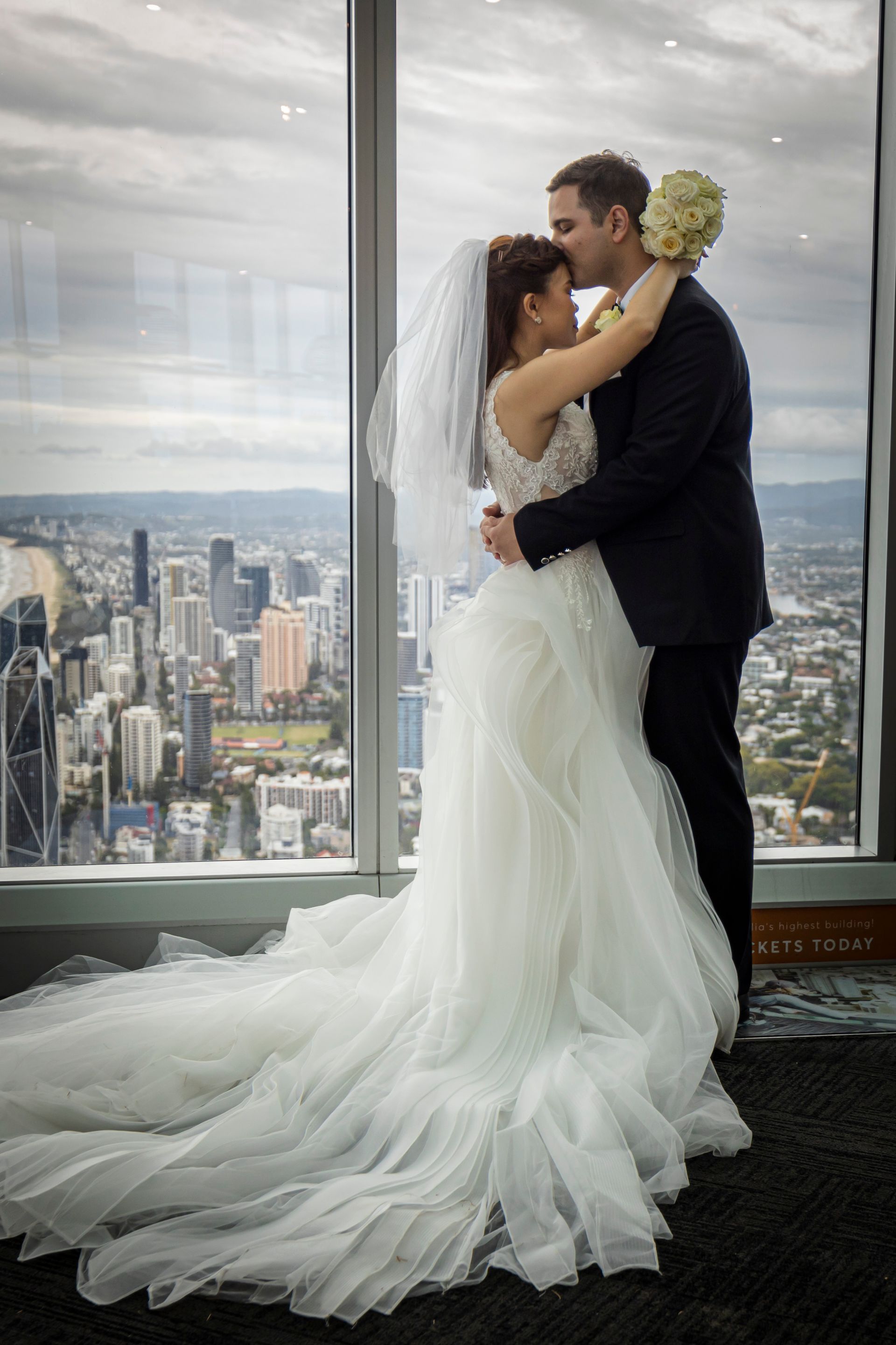 a bride and groom are kissing in front of a window overlooking a city .
