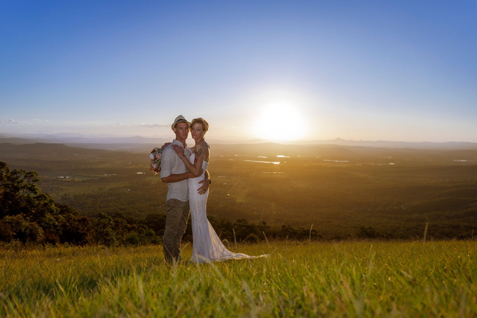 a bride and groom are standing in a field at sunset .