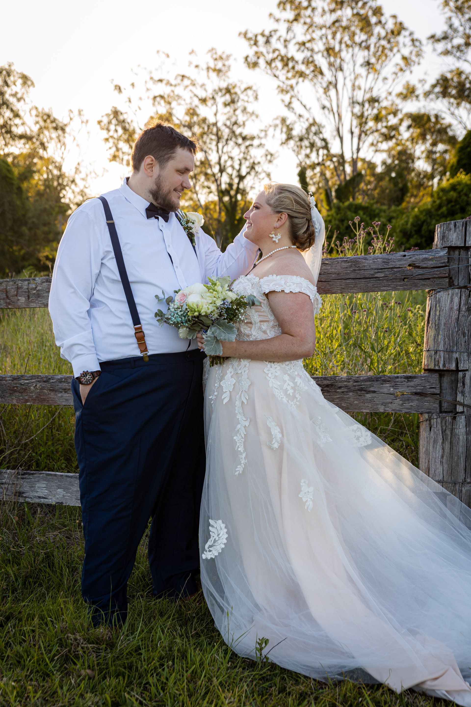 a bride and groom are posing for a picture in front of a wooden fence .