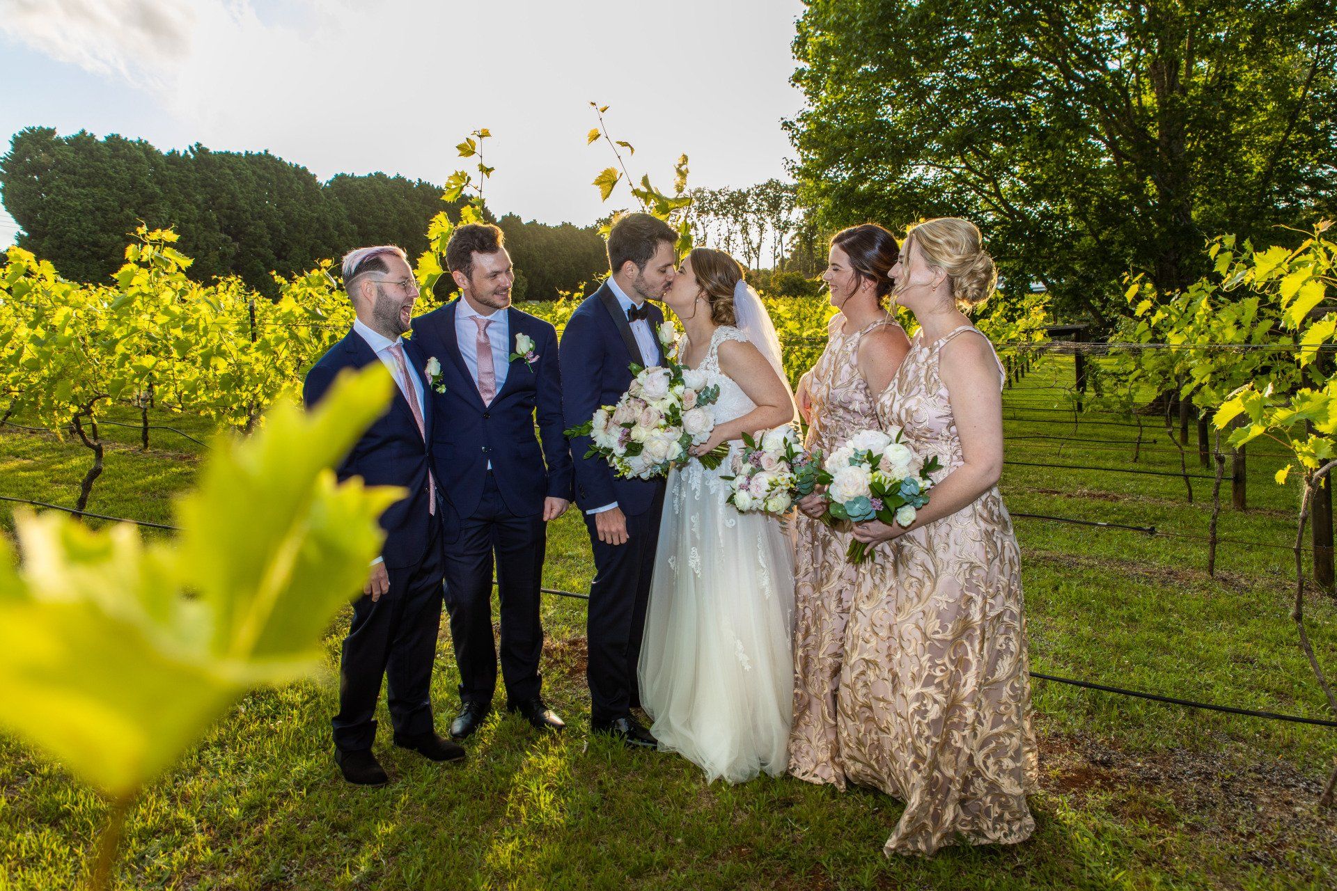 a bride and groom are posing for a picture with their wedding party in a vineyard .
