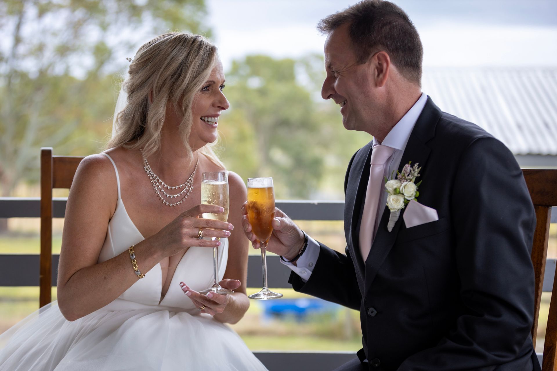 a bride and groom are sitting on a bench toasting with champagne glasses .