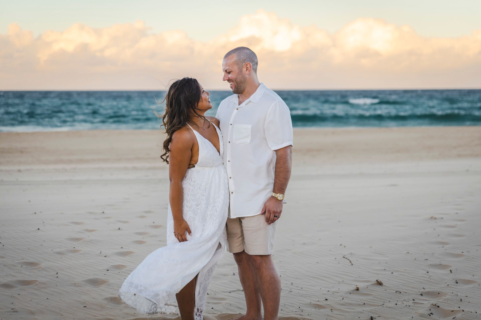 a man and a woman are standing on a beach looking at each other .