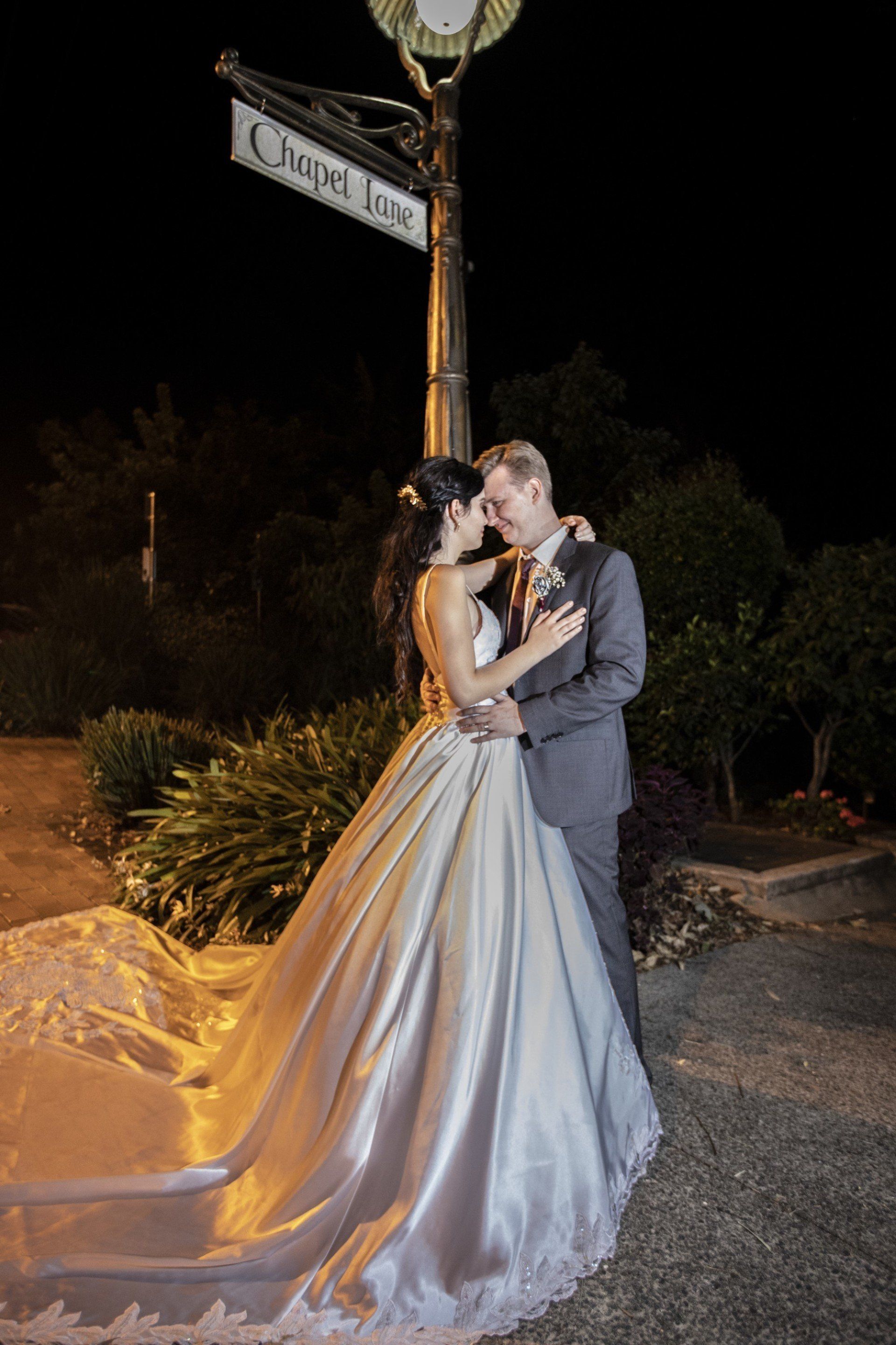 a bride and groom are posing for a picture in front of a clock at night .
