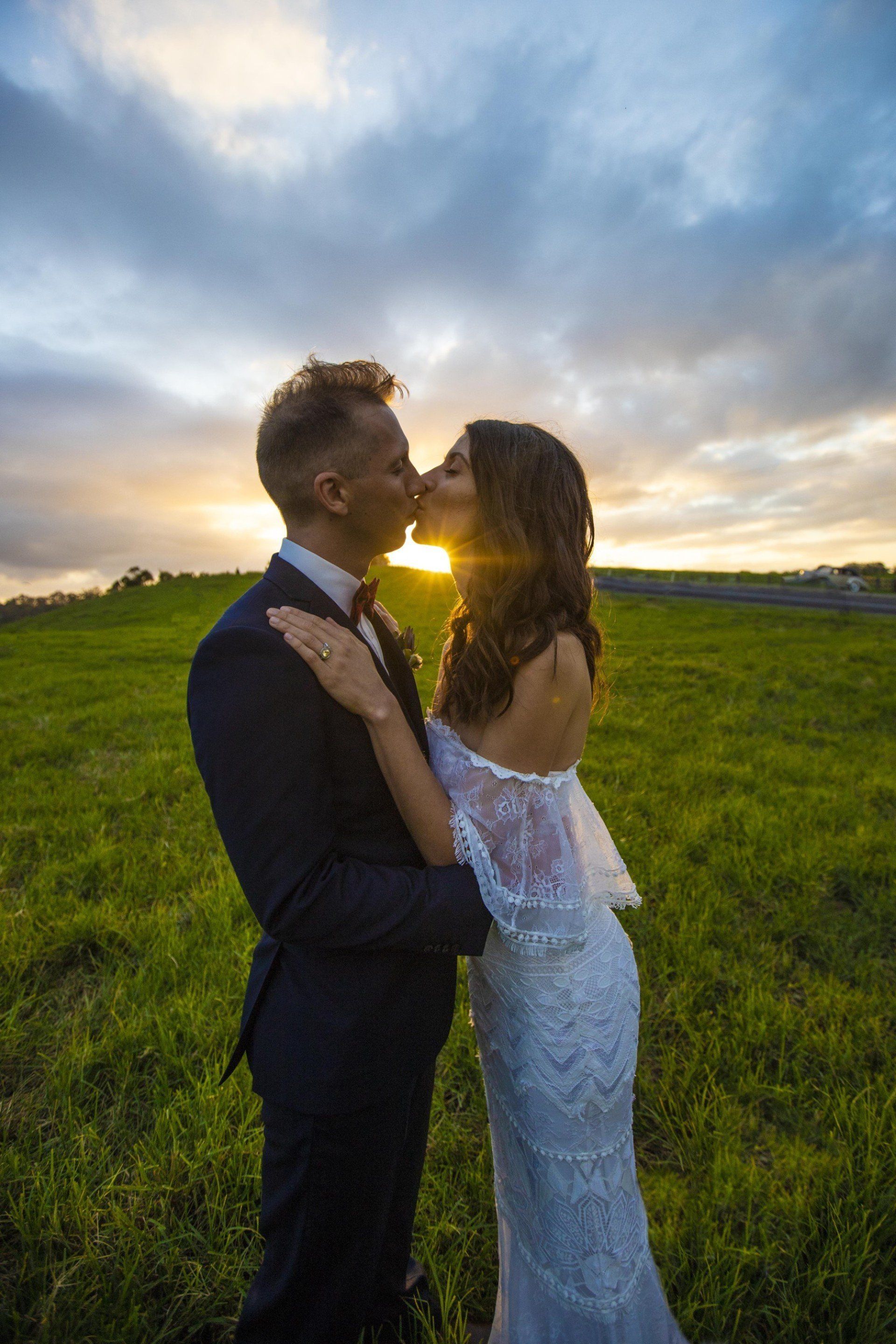 a bride and groom are kissing in a field at sunset .