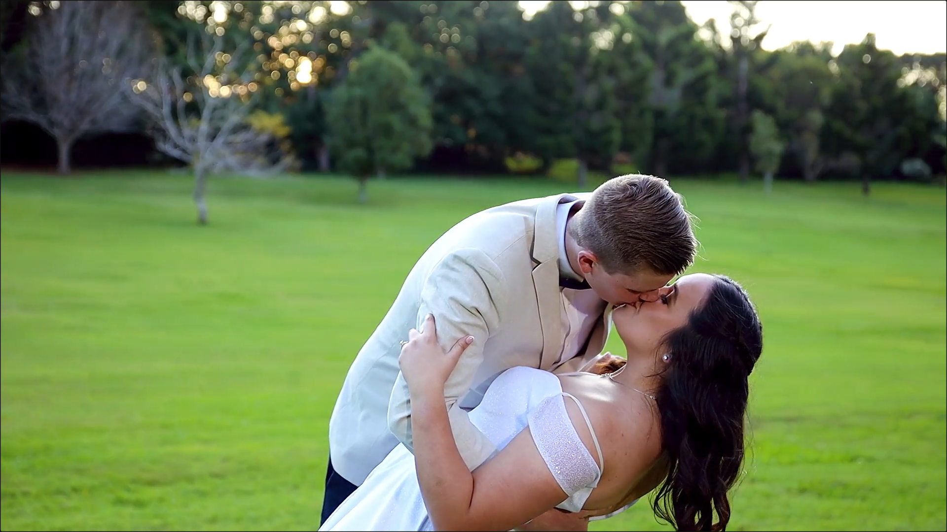 a bride and groom are kissing in a field .