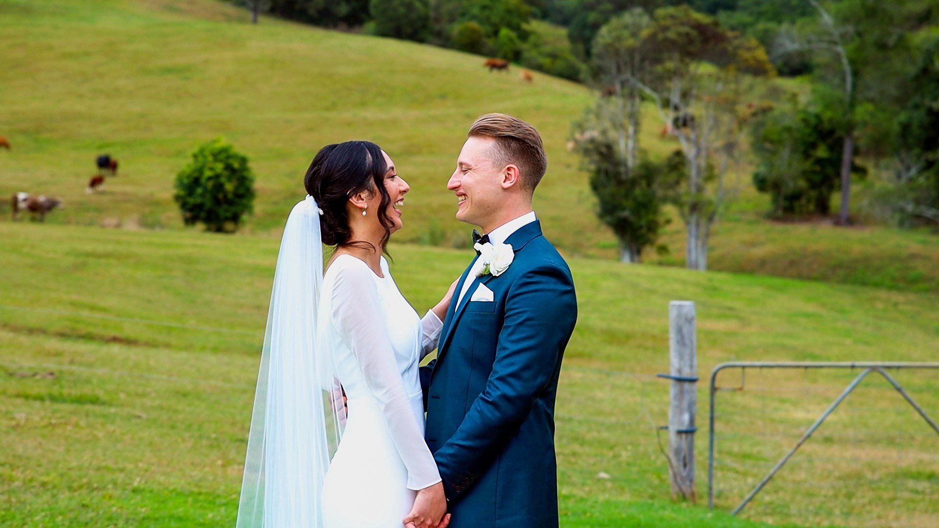 a bride and groom are standing in a grassy field holding hands .